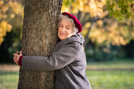 171146075-belle-femme-âgée-étreignant-un-arbre-dans-le-parc-femme-mature-étreignant-un-arbre-et-souriant-en