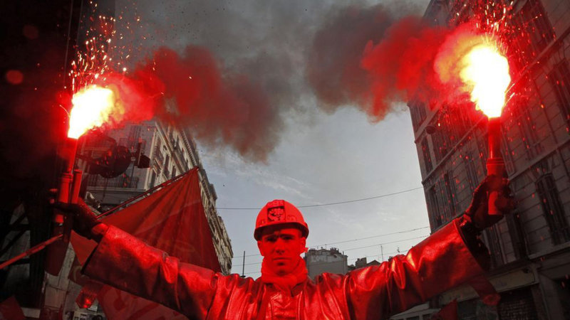 Attali-an-arcelor-mittal-steel-worker-dressed-in-a-protective-work-suit-holds-flares-as-he-demonstrates-over-pension-reforms-in-marseille_2440080