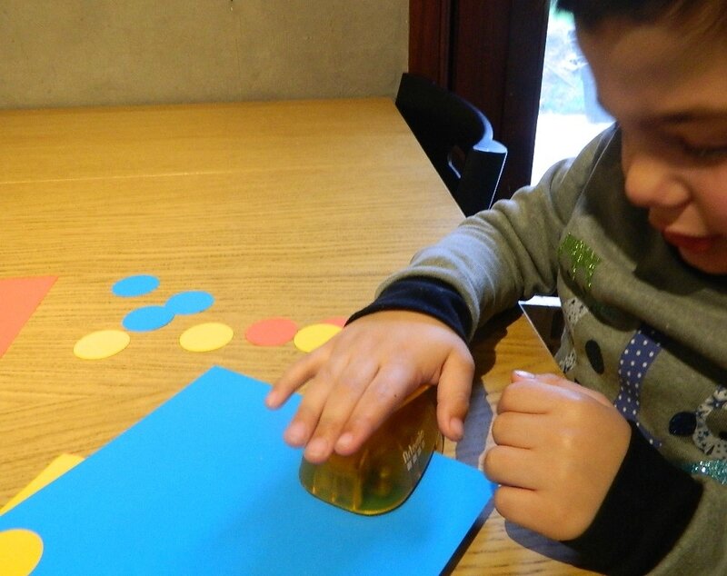 un enfant utilise une perforatrice pour découper des ronds dans des feuilles bleu, jaunes et rouges