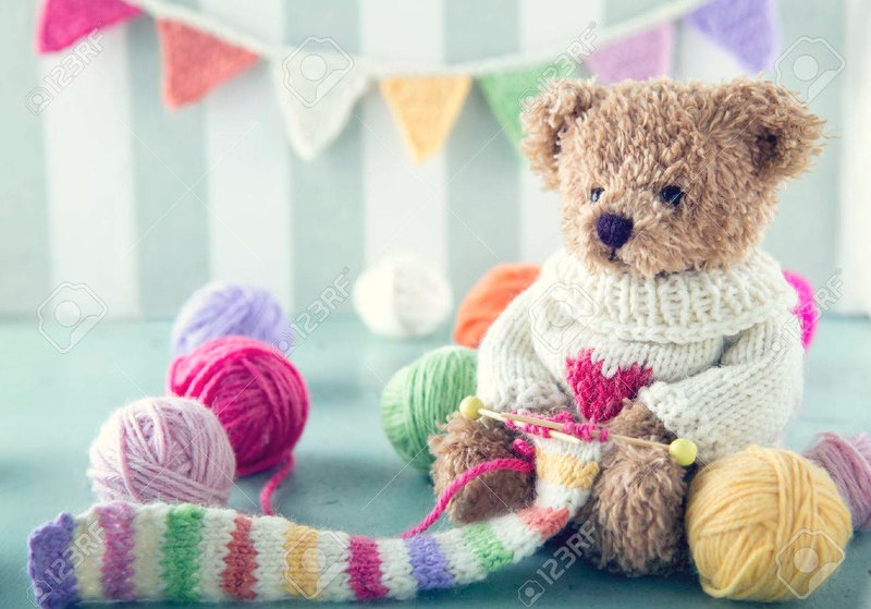 64798604-ours-en-peluche-dans-un-chandail-de-laine-à-tricoter-une-écharpe-rayée-avec-des-boules-colorées-de