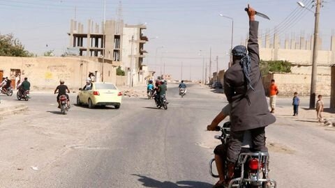 man-holds-up-a-knife-as-he-rides-on-the-back-of-a-motorcycle-touring-the-streets-of-tabqa-city-with-others-in-celebration-after-islamic-stat